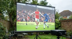 Close-up of a high-lumen outdoor projector screen displaying vibrant football match highlights in daylight.