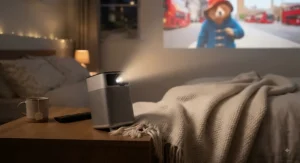 Close-up of a small projector for bedroom placed next to a soft throw blanket
