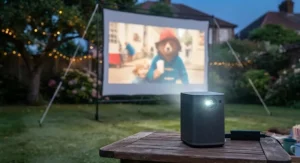 Close-up of a portable battery-powered projector projecting onto an outdoor garden cinema projector screen.